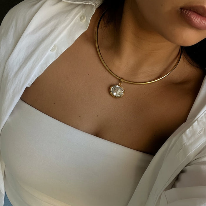 Close-up of a person wearing a white garment with a gold hoop earring and diamond pendant.