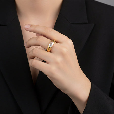 Hand wearing a gold ring with a diamond, against a black background