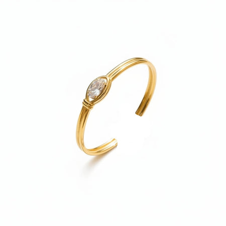 Gold bracelet with a clear gemstone on a person's wrist against a neutral background